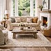 Floral upholstered sofa in a light-filled living room with open French doors leading to a garden, styled with neutral cushions, a rustic coffee table, and a fireplace.